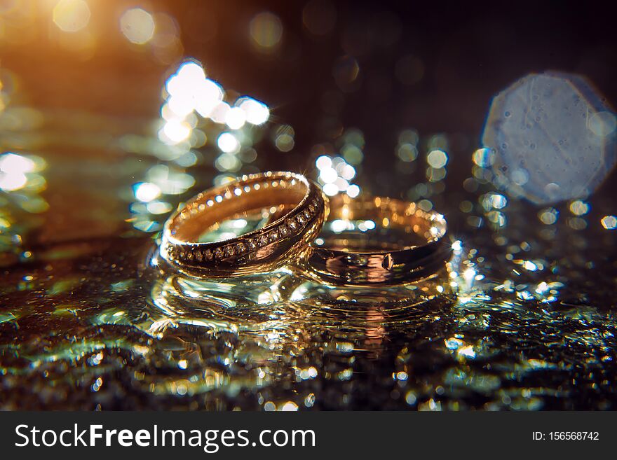 Gold wedding rings of bride and groom in shiny water spray, bright background, selective focus. Wedding accessories and jewelry