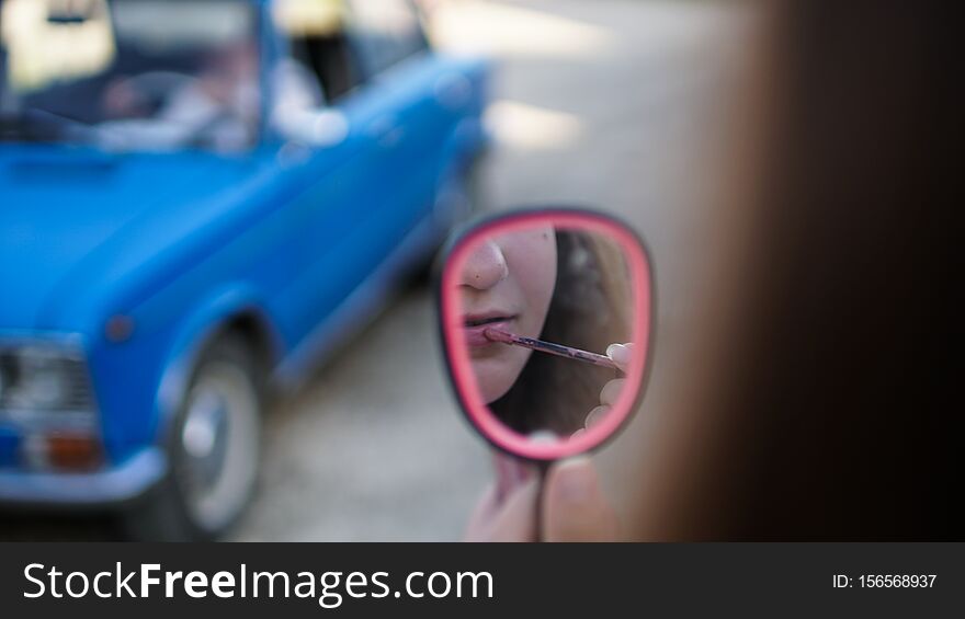 Young woman draw lips with red pencil looking in the mirror