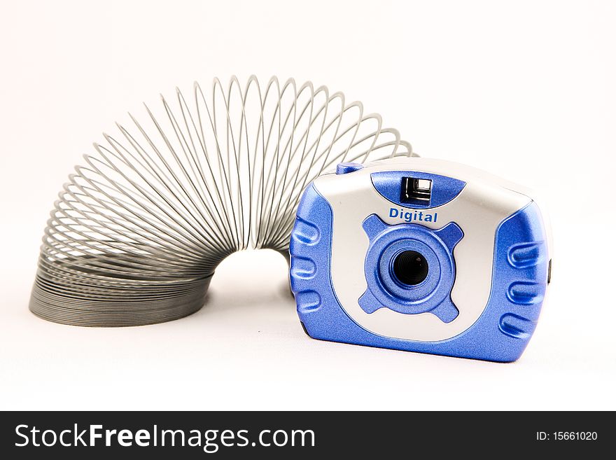 A blue and silver digital camera with a strewn out silver slinky. A blue and silver digital camera with a strewn out silver slinky