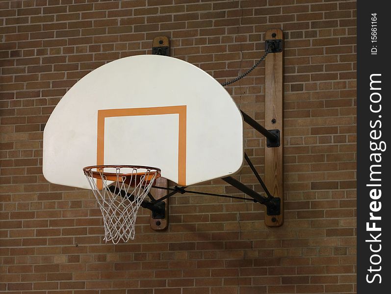 A basketball hoop on the wall in an old brick school gym or gymnasium. A basketball hoop on the wall in an old brick school gym or gymnasium.