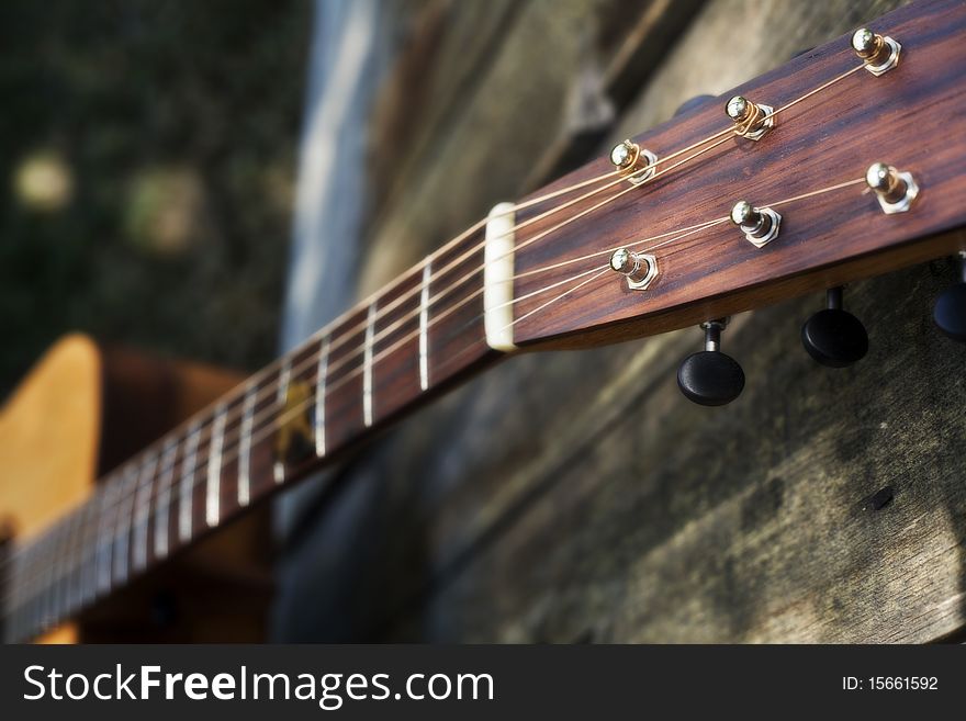 This is a picture of a traditional acoustic custom guitar's fret board resting against a faded fence. This is a picture of a traditional acoustic custom guitar's fret board resting against a faded fence.