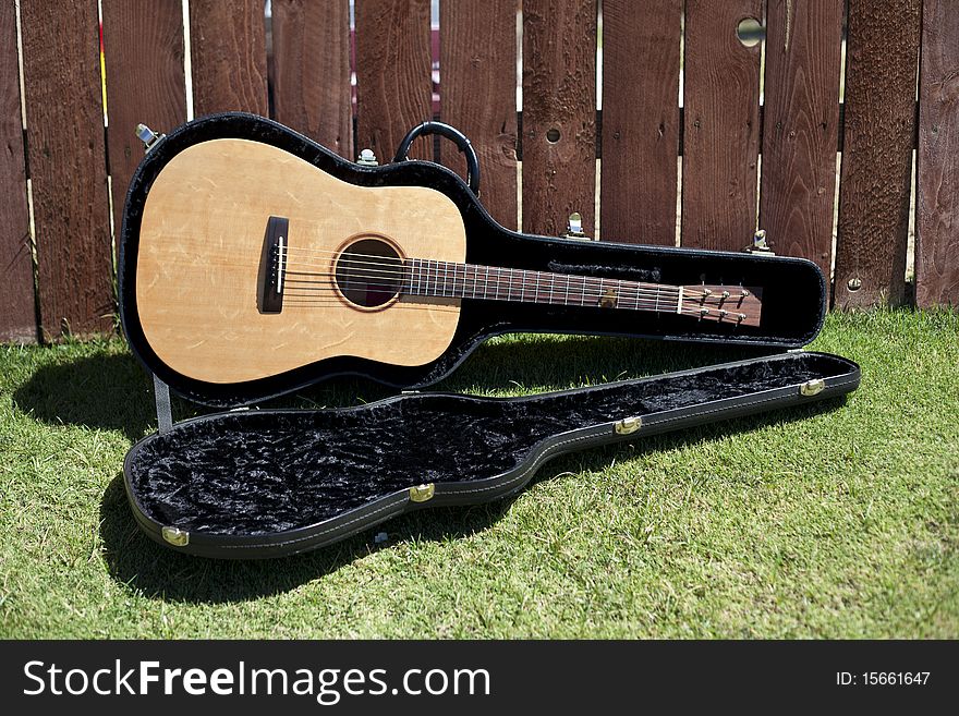 This is a picture of an acoustic guitar in a case against a redwood fence. This is a picture of an acoustic guitar in a case against a redwood fence.