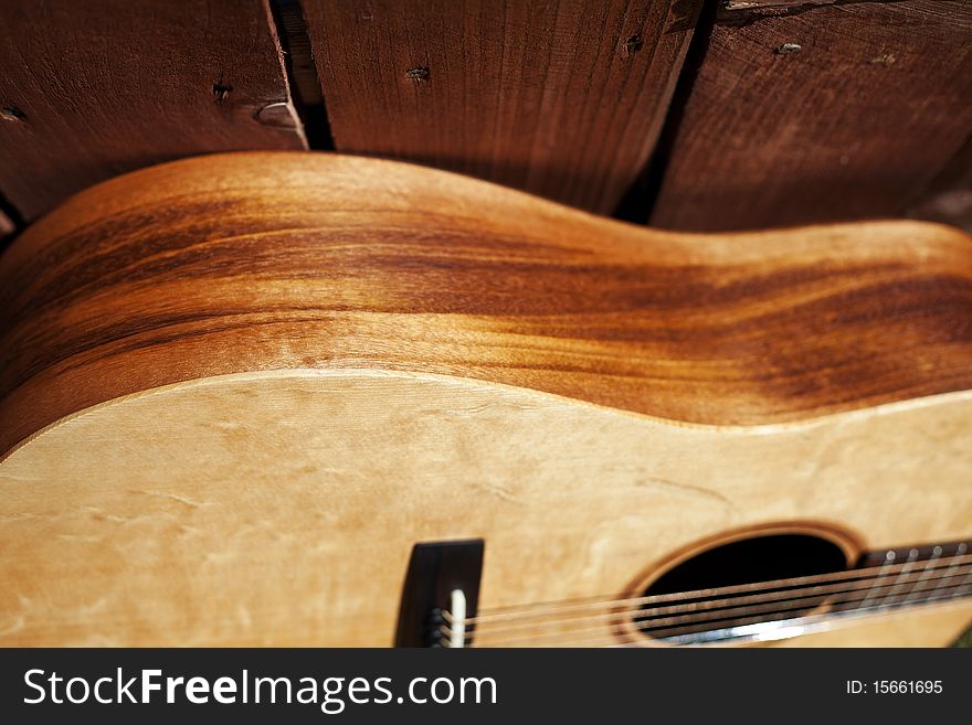 This is a picture of the side of an acoustic guitar against a redwood fence with a long view of the fence. This is a picture of the side of an acoustic guitar against a redwood fence with a long view of the fence..