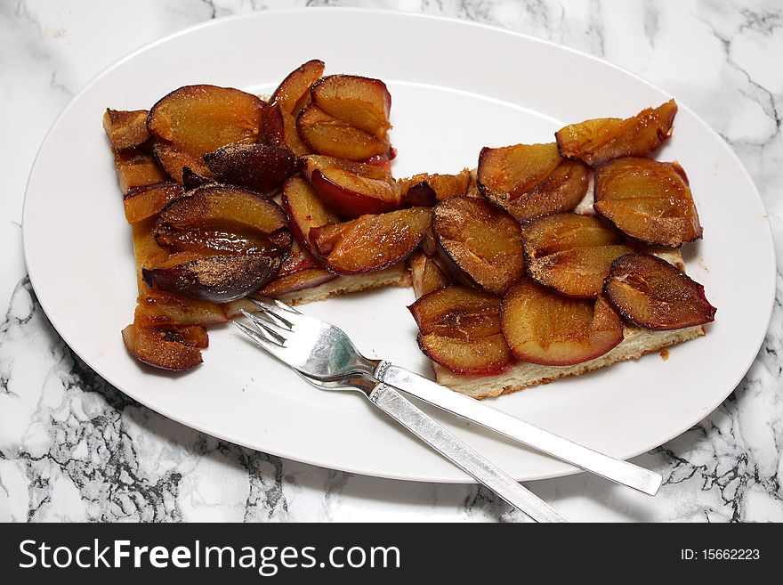 Two servings of fresh plum cakes from yeast dough on a white record with two pastry forks to the immediate consumption.