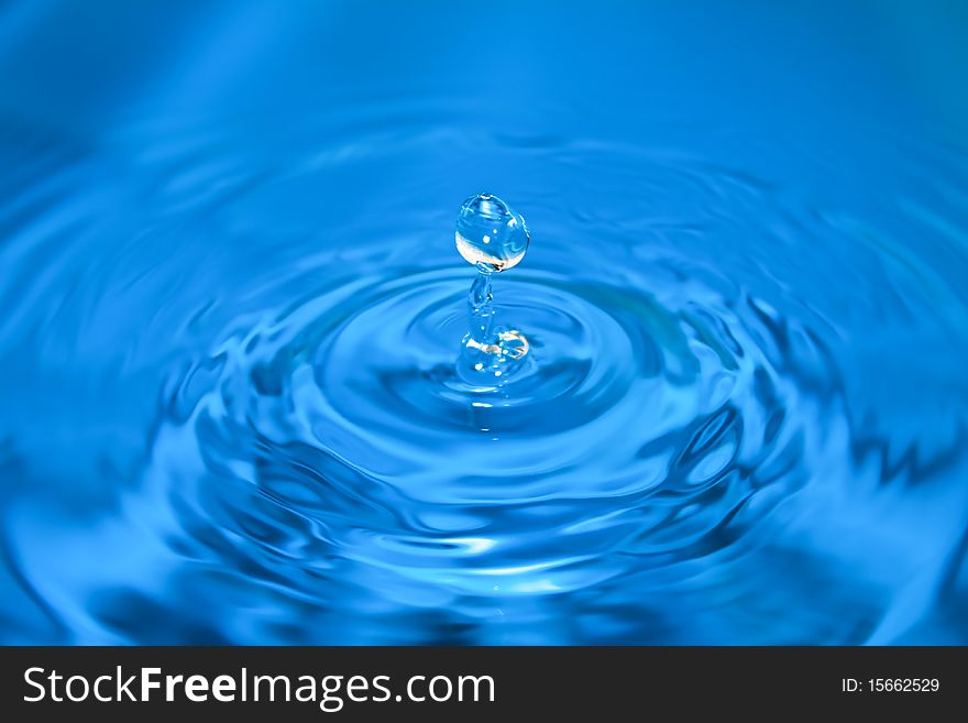 Clean blue drop of water splashing in clear water. Abstract blue background