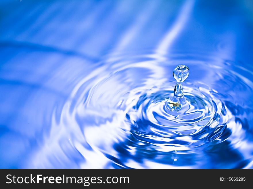 Clean blue drop of water splashing in clear water. Abstract blue background