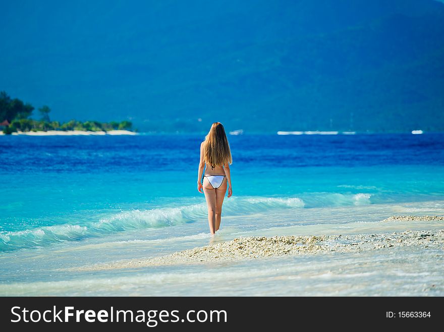 A beautiful woman wearing white bikini facing the sea on a vacant beach in paradise