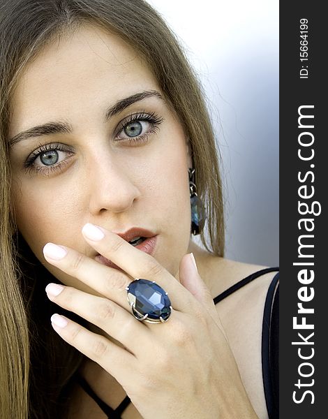 Portrait of elegantly beautiful young woman covers her mouth with his hand. The girl beautiful jewelry, ring and earrings with large blue stones. Portrait of elegantly beautiful young woman covers her mouth with his hand. The girl beautiful jewelry, ring and earrings with large blue stones