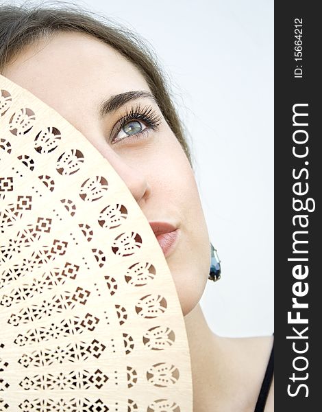 Beautiful young fashion girl with a wooden fan that covers half her face. Beautiful young fashion girl with a wooden fan that covers half her face