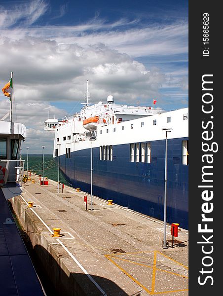 Quayside with a large blue and white ship in dock. Life belts, tie up points and lights are on the quay. Quayside with a large blue and white ship in dock. Life belts, tie up points and lights are on the quay.