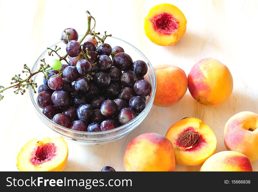 A vine and peaches lie in a dish. A vine and peaches lie in a dish