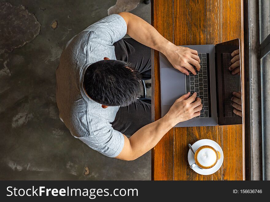 Muscled Asian man typing laptop next to cup of cappuccino