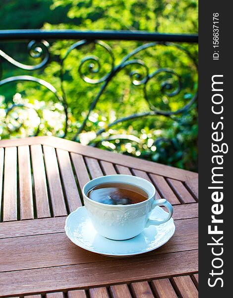 Single white ceramic cup of tea on a saucer on wooden table against picturesque and natural green foliage background. Single white ceramic cup of tea on a saucer on wooden table against picturesque and natural green foliage background.