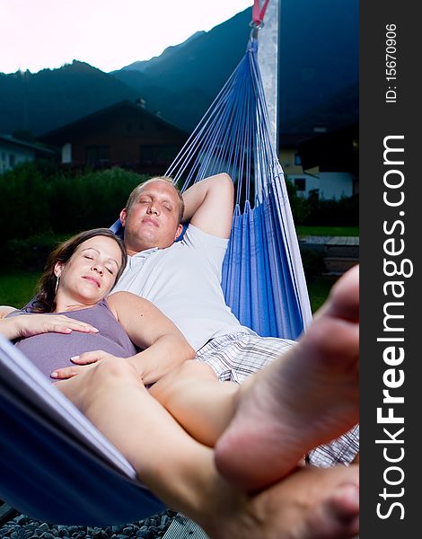 Young loving couple in a hammock in a summer setting. The woman is pregnant. Young loving couple in a hammock in a summer setting. The woman is pregnant.