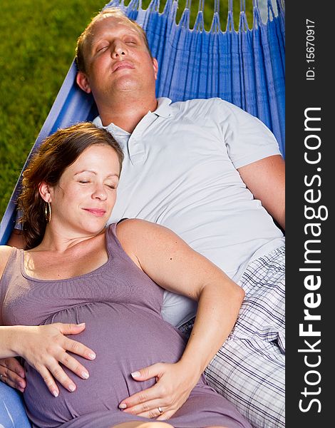 Young loving couple in a hammock in a summer setting. The woman is pregnant. Young loving couple in a hammock in a summer setting. The woman is pregnant.