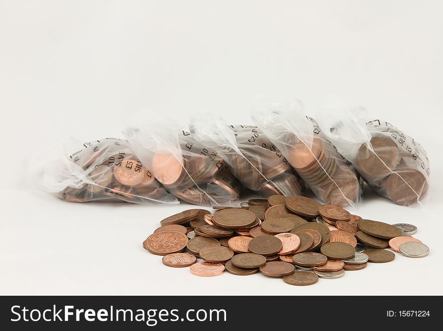 A pile of loose coins with bags of coins in the background isolated on white. A pile of loose coins with bags of coins in the background isolated on white.