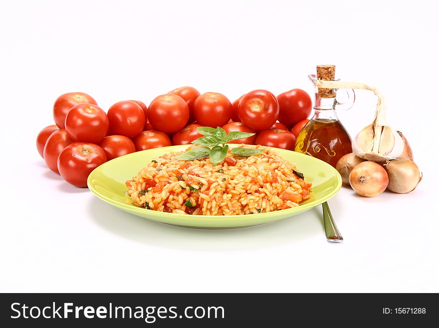 Risotto with tomatoes on a green plate decorated with basil with fresh tomatoes, onions, garlic and olive oil on white background