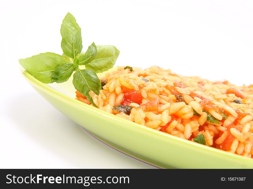 Risotto with tomatoes on a green plate decorated with basil in close up