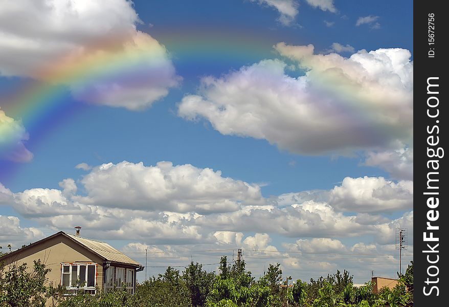 Rainbow and summers cloudy sky above a building and trees