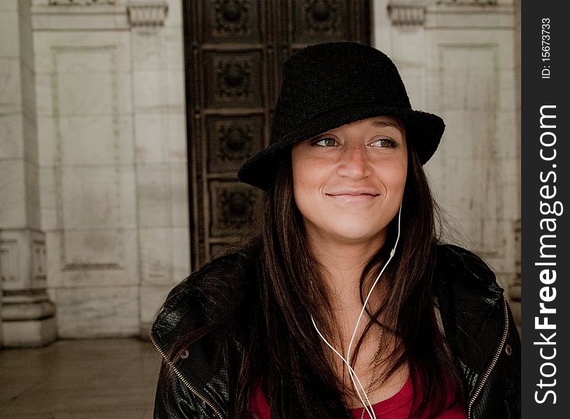 Beautiful young woman with a fedora listening to portable music player in an urban city. Beautiful young woman with a fedora listening to portable music player in an urban city.