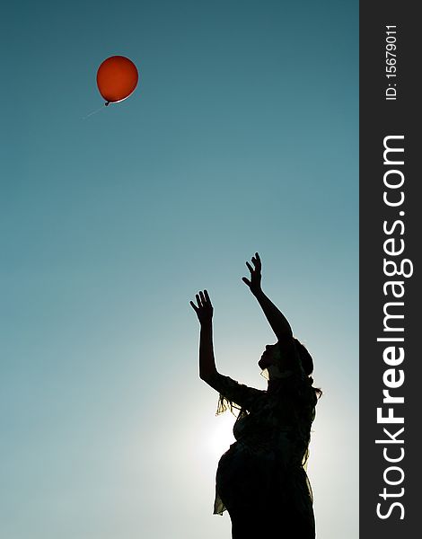 A silhouette of a pregnant woman in her 9th month throwing a red balloon into the blue sky
