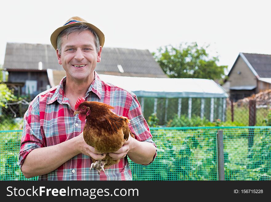 Mature Farmer Wearing Hat While Carrying Chicken Against Barn