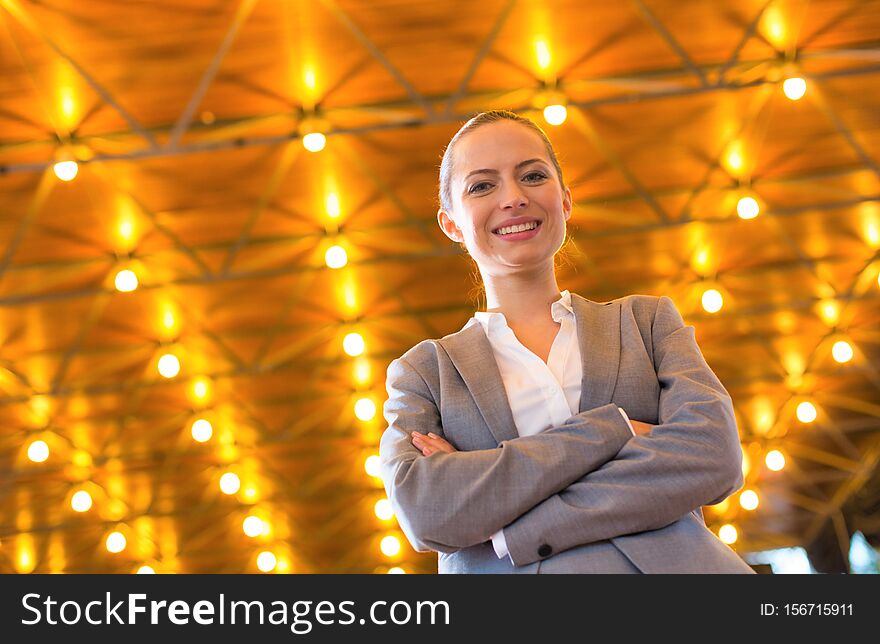 Photo of Confident young businesswoman standing with arms crossed against illuminated roof