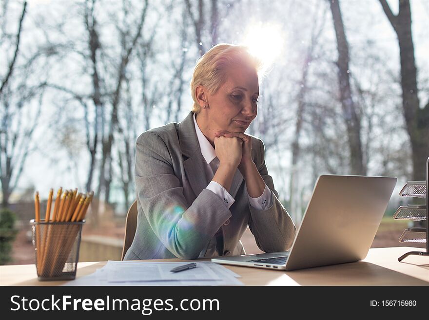 Confident mature businesswoman sitting with laptop at desk against window in office