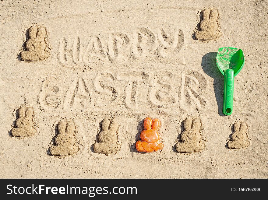 Text Happy Easter and several Easter bunnieas are on the sand. Text Happy Easter and several Easter bunnieas are on the sand