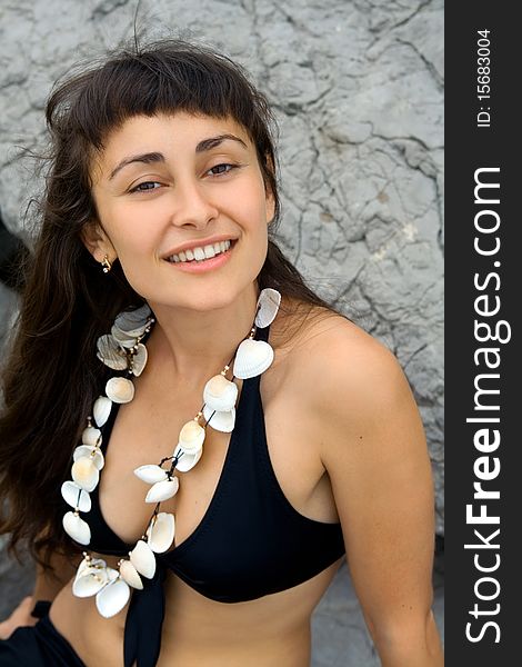 Portrait of a young pretty girl in the bathing suit with seashell beads near the rocks on the seashore. Portrait of a young pretty girl in the bathing suit with seashell beads near the rocks on the seashore