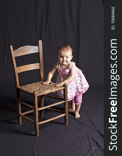 Baby girl posing next to old chair, studio shot. Baby girl posing next to old chair, studio shot