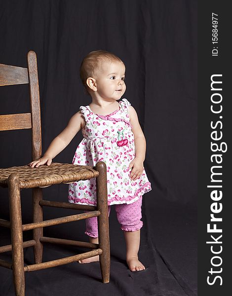 Baby girl posing next to old chair, studio shot. Baby girl posing next to old chair, studio shot