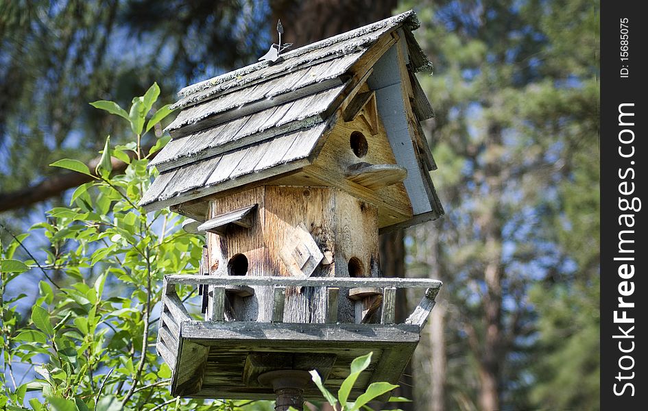 A close-up of a handmade wooden birdhouse with shingled roof and a forest in the background. A close-up of a handmade wooden birdhouse with shingled roof and a forest in the background.