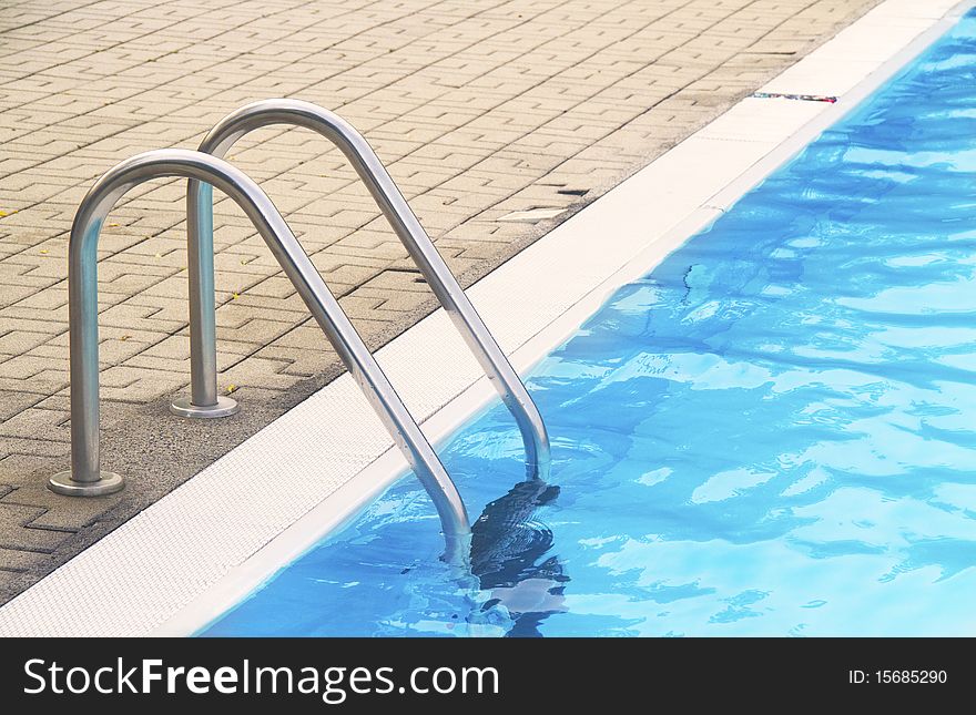 Stainless steel pool ladder goes down into blue water