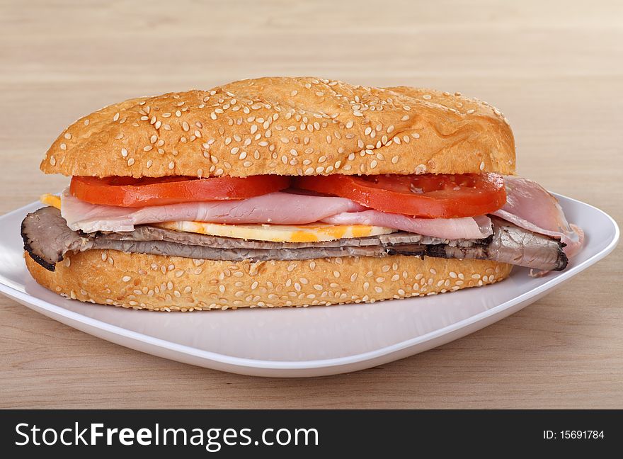 Ham and roast beef sub with tomatoes and cheese on a sesame seed bun. Ham and roast beef sub with tomatoes and cheese on a sesame seed bun