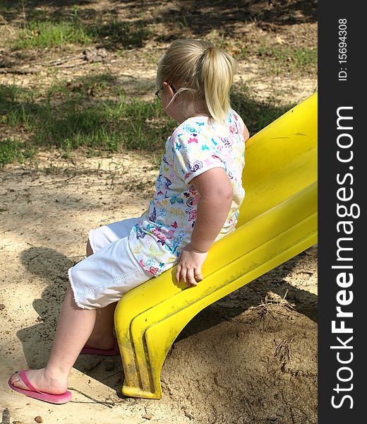 little girl sitting on a yellow slide at playground looking at her own shadow. little girl sitting on a yellow slide at playground looking at her own shadow...