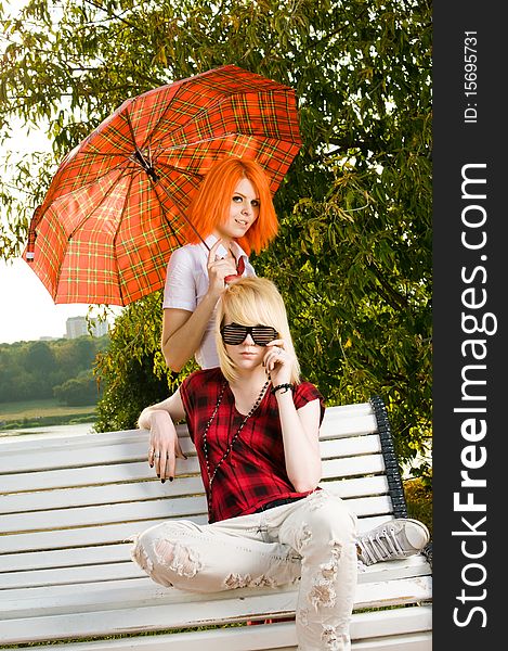 Two teenage girls sitting on a bench at the summer park. Two teenage girls sitting on a bench at the summer park