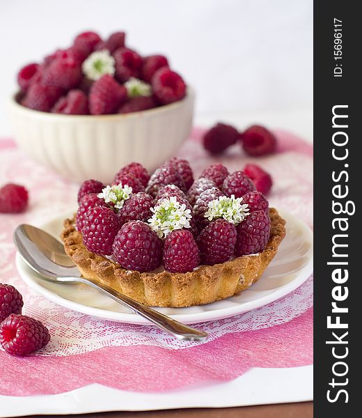 A fresh raspberry tart on a napkin and bowl of raspberries in background