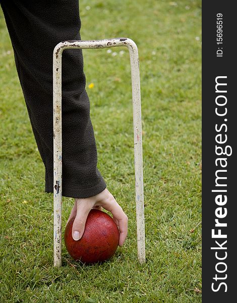 Hand picking up a red croquet ball through the hoop. Hand picking up a red croquet ball through the hoop