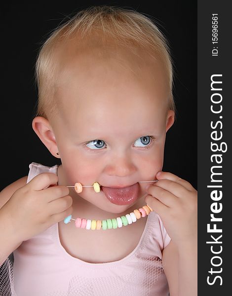 Cute blond baby girl eating a candy necklace. Cute blond baby girl eating a candy necklace