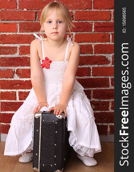 Beautiful little girl sitting on a suitcase. Travel ballet dancer