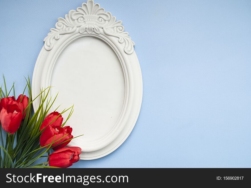 White Photo Frame On A Blue Background With Red Flowers. Flat Lay.