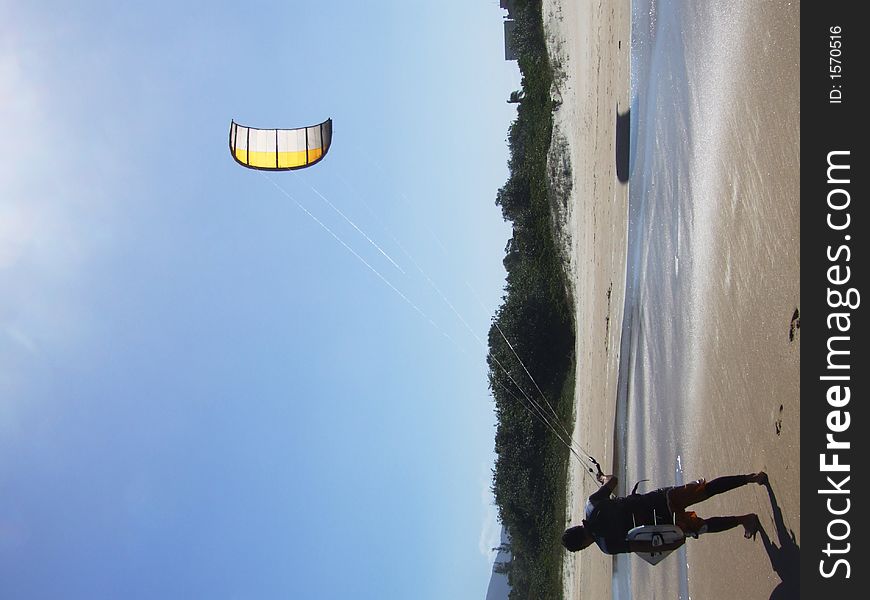 Kite surfer on the beach in Brazil. Yellow kite against blue sky.