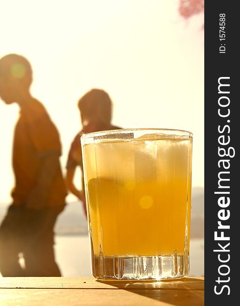 Ka glass of orange juice with children holding hands in the background. Ka glass of orange juice with children holding hands in the background