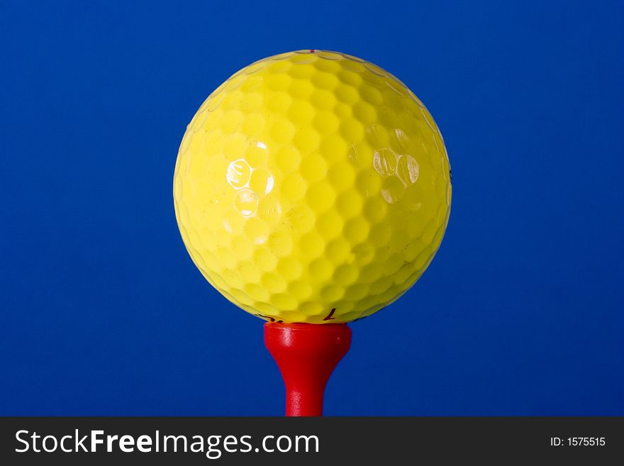 Yellow Golf ball on red tee against blue background photographed in studio