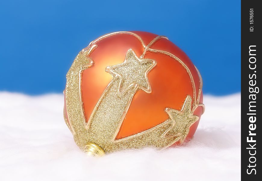 Orange christmas ball arranged with golden ornaments on white fluffy surface over blue background