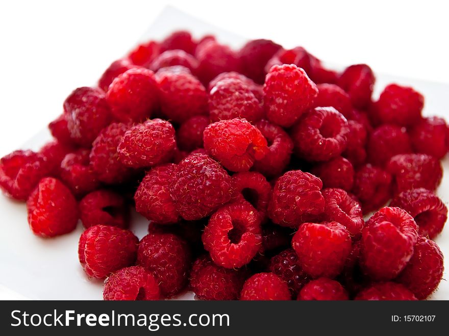 A heap of red raspberries on plate. White background. A heap of red raspberries on plate. White background