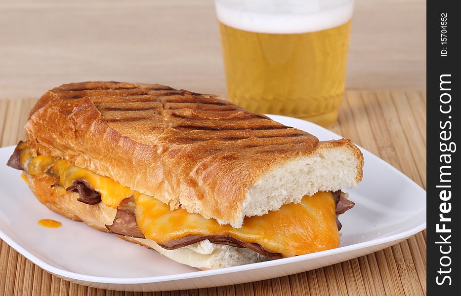 Roast beef sandwich covered with melted cheese on grilled French bread and a beverage. Roast beef sandwich covered with melted cheese on grilled French bread and a beverage