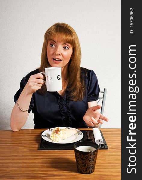 A vertical image of a pretty young woman in a cafe setting having lunch of coffee and a delicious cream cake and trying to attract the attention of someone to join her. A vertical image of a pretty young woman in a cafe setting having lunch of coffee and a delicious cream cake and trying to attract the attention of someone to join her
