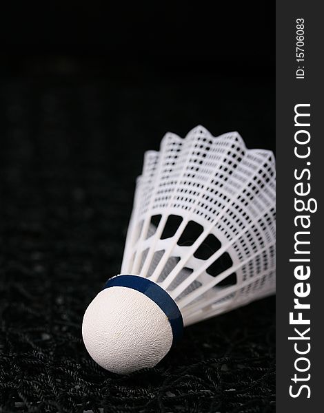 Close-up of a white synthetic shuttlecock on a black badminton net.